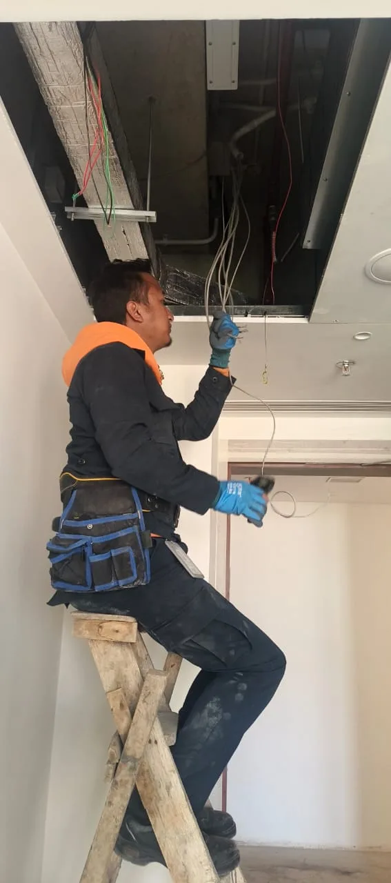 A technician on a ladder pulling network cable through an open ceiling panel