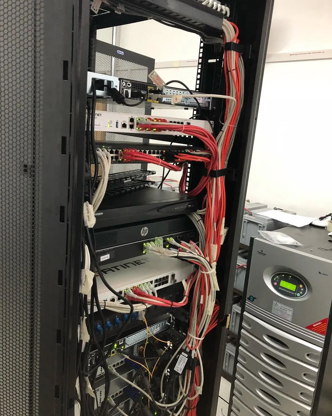 Equipment rack containing a firewall, switches, a CCTV recorder and patch cabling beside a UPS unit
