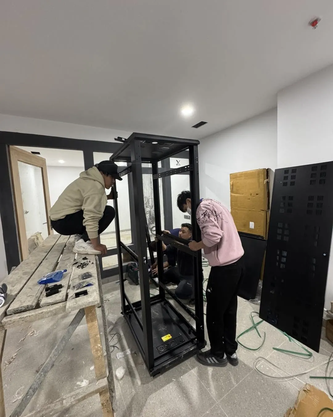 aBit technicians assembling a black equipment rack frame in an unfinished server room