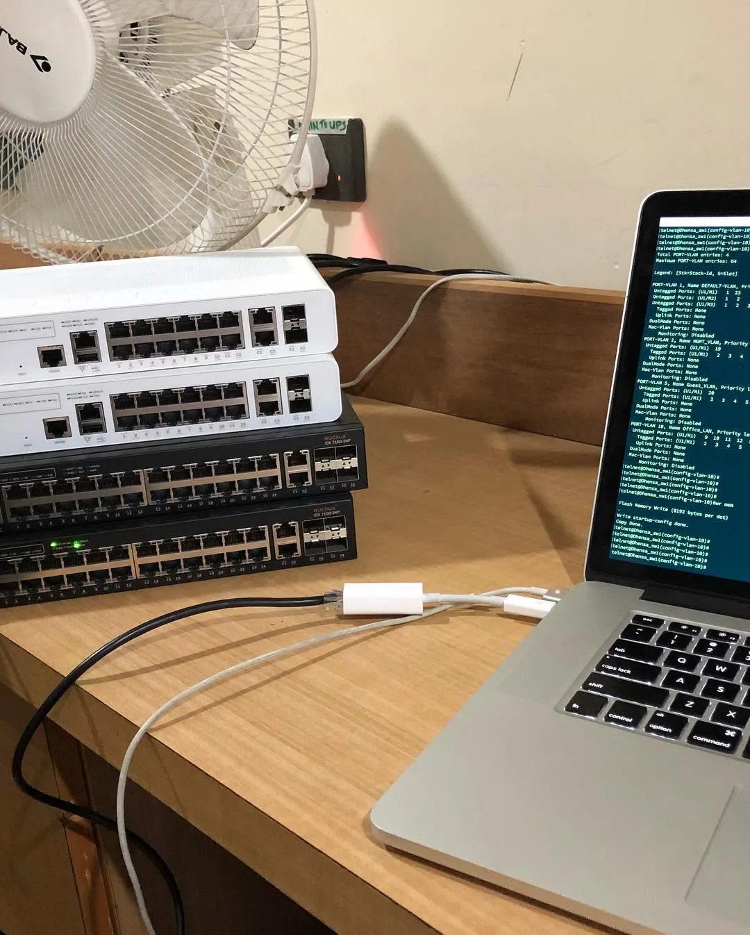 Stacked network switches connected to a laptop showing VLAN configuration output during setup