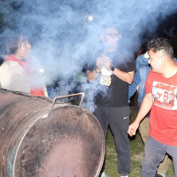 Grilling over a drum barbecue at an evening gathering