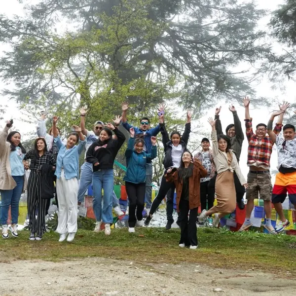The team jumping for a photo beside a line of prayer flags on a misty ridge