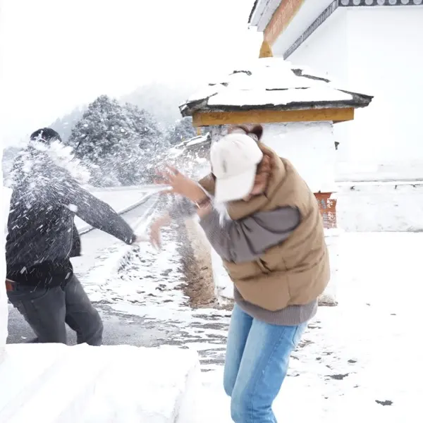 A snowball fight in fresh snow beside a whitewashed temple wall